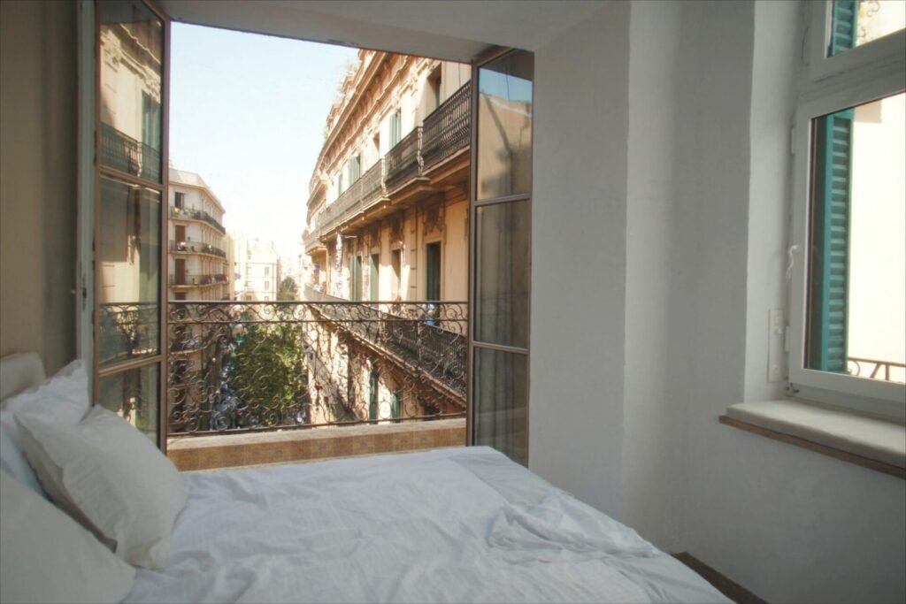 Bright hotel balcony in the Eixample with white linen and open doors